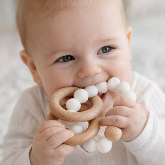 Baby chewing natural wooden and white silicone teether ring, neutral baby teething toy for sore gums, safe BPA-free silicone bead teether for infants.