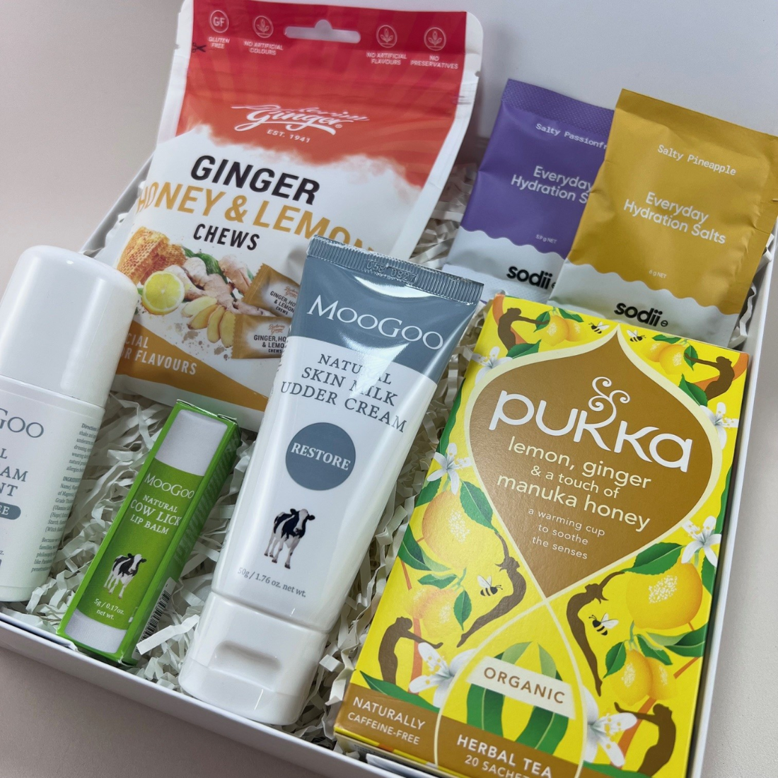 Close-up of Cancer Care Mini Gift Box contents including MooGoo sensitive lip balm, udder lotion, deodorant, ginger chews, herbal tea and hydration salts