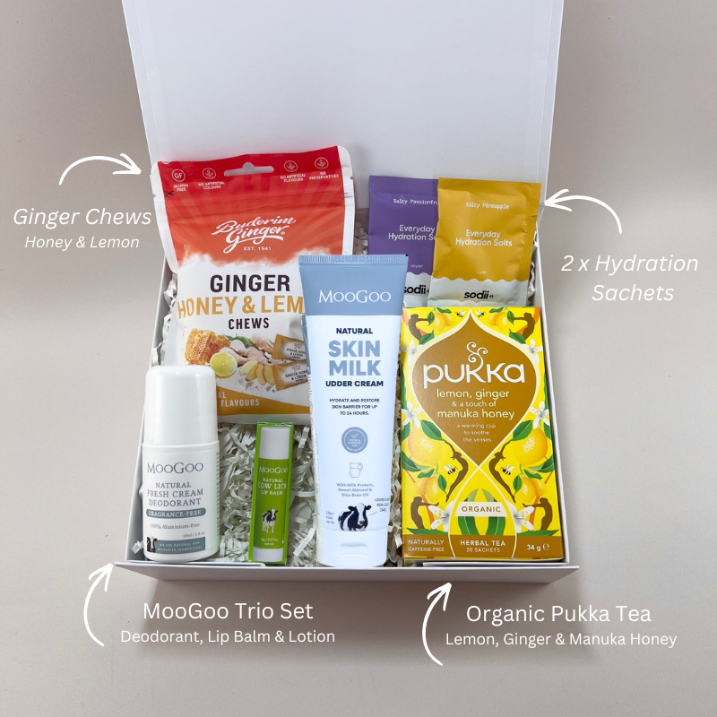 Chemotherapy care gift box laid out with MooGoo skin milk lotion, sensitive lip balm, Buderim ginger chews with honey and lemon, Pukka organic tea and Sodii hydration sachets. With labels.