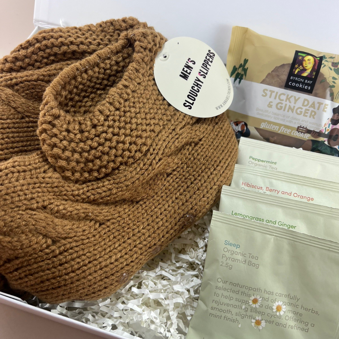 Close-up of the Mini Comforts Care Package in a white gift box, featuring cosy socks, Love Tea sachets and a gluten-free cookie