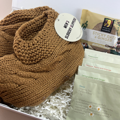 Close-up of the Mini Comforts Care Package in a white gift box, featuring cosy socks, Love Tea sachets and a gluten-free cookie