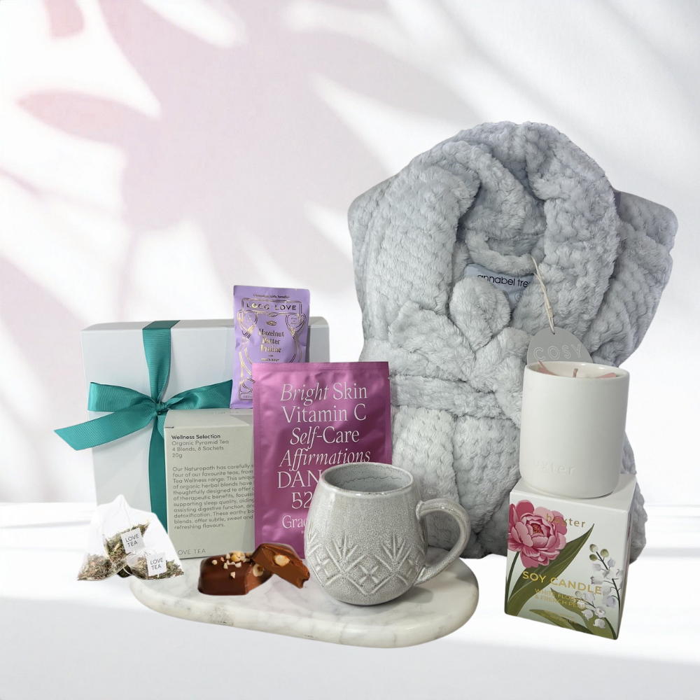 Cosy Self-Care Retreat gift box with a grey plush robe, organic wellness tea selection, textured stoneware mug, soy candle, chocolate pieces and face mask displayed on a marble tray