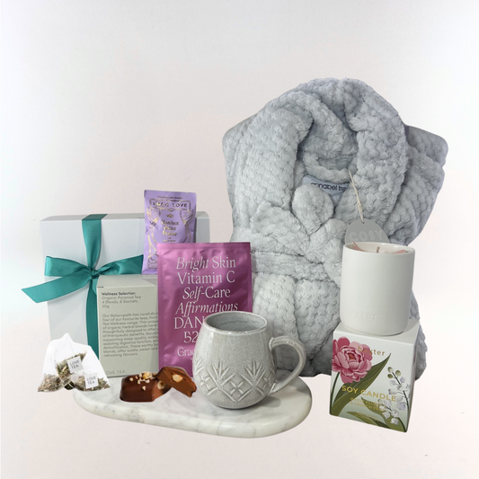 Cosy Self-Care Retreat gift box with a grey plush robe, organic wellness tea selection, textured stoneware mug, soy candle, chocolate pieces and face mask displayed on a marble tray