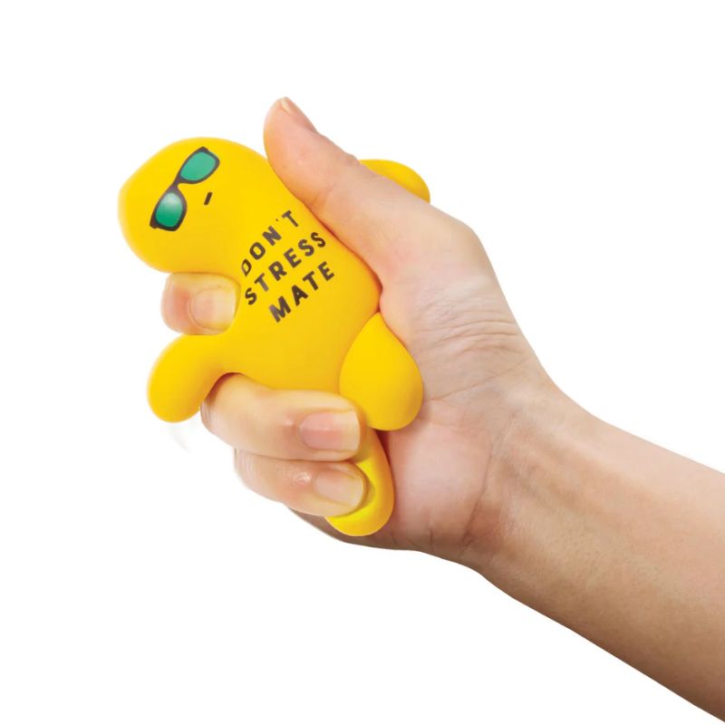 A hand squeezing a small yellow stress toy shaped like a person wearing green sunglasses, with the text 'DON'T STRESS MATE' printed on the side, against a plain white background.