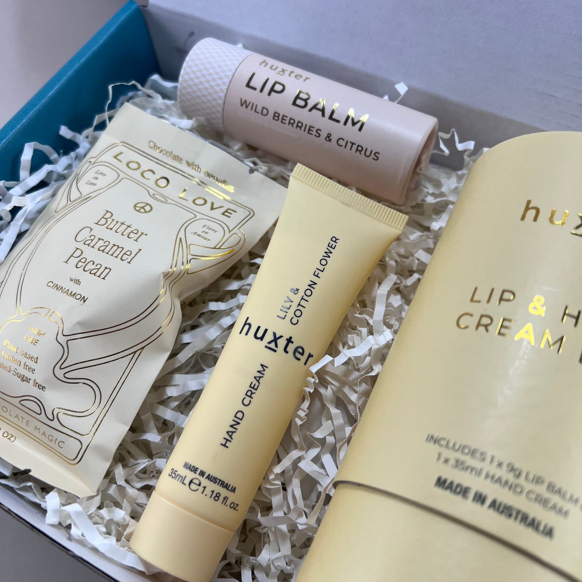 Close-up of Loco Love butterscotch caramel truffle bar and Huxter lip balm and hand cream, displayed together in a gift box.