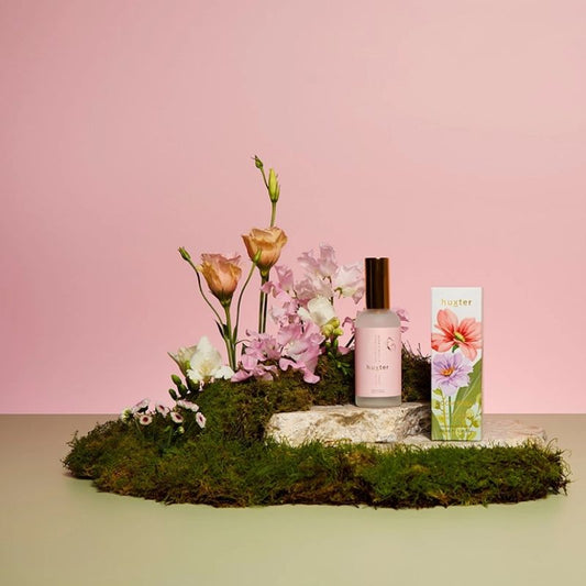 Huxt er White Florals & French Pear room spray 100ml displayed with pink flowers and moss styling on pastel background.