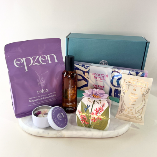 A curated wellness gift set arranged on a white marble tray against a light neutral background. The set includes an Epzen Relax magnesium epsom salt pouch, 