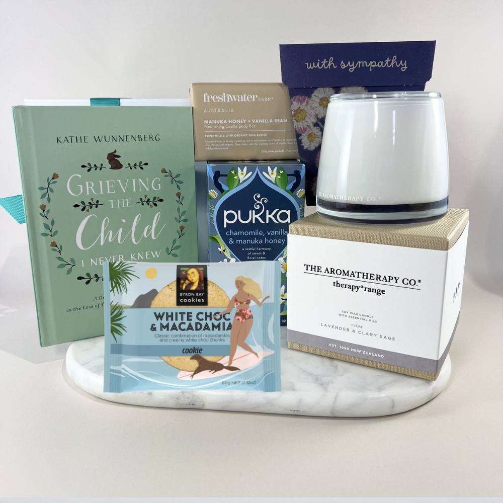 Thinking of You sympathy gift box with a calming lavender candle, forget-me-not seed packet, chamomile herbal tea, manuka honey soap bar, white chocolate macadamia cookie and a "With Sympathy" card on a marble tray. Includes Greving the child book.
