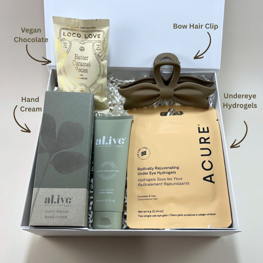 Close up of Treat Yourself gift box showing Al.ive Body ivory bloom hand cream tube and box, Acure under eye hydrogel packet, trendy bow claw clip and Loco Love chocolate