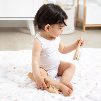 Baby sitting on blanket holding natural wooden baby brush with soft bristles