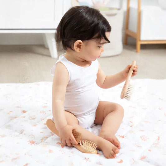 Baby sitting on blanket holding natural wooden baby brush with soft bristles