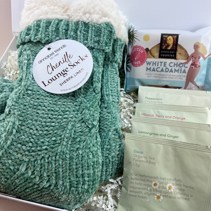 Close up of Mini Comforts Care Package contents laid out; sherpa socks, four organic tea sachets, and a Byron Bay Cookies white choc macadamia cookie