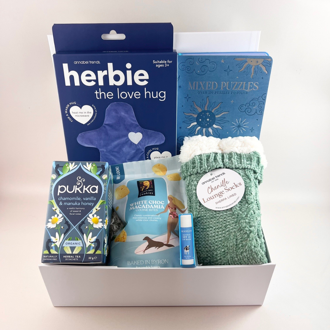 The Big Hug Bundle — a recovery gift box containing Herbie the Love Hug heat and cold therapy pillow, a mixed puzzle book, Pukka calming herbal tea, Byron Bay white chocolate and macadamia cookies, MooGoo SPF15+ lip balm, and sherpa lined grip socks.