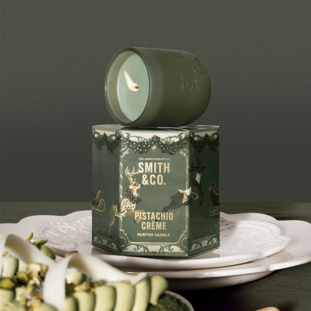 Smith & Co. Pistachio Crème candle on its hexagonal gift box, set on a white cake stand with pistachio pastries