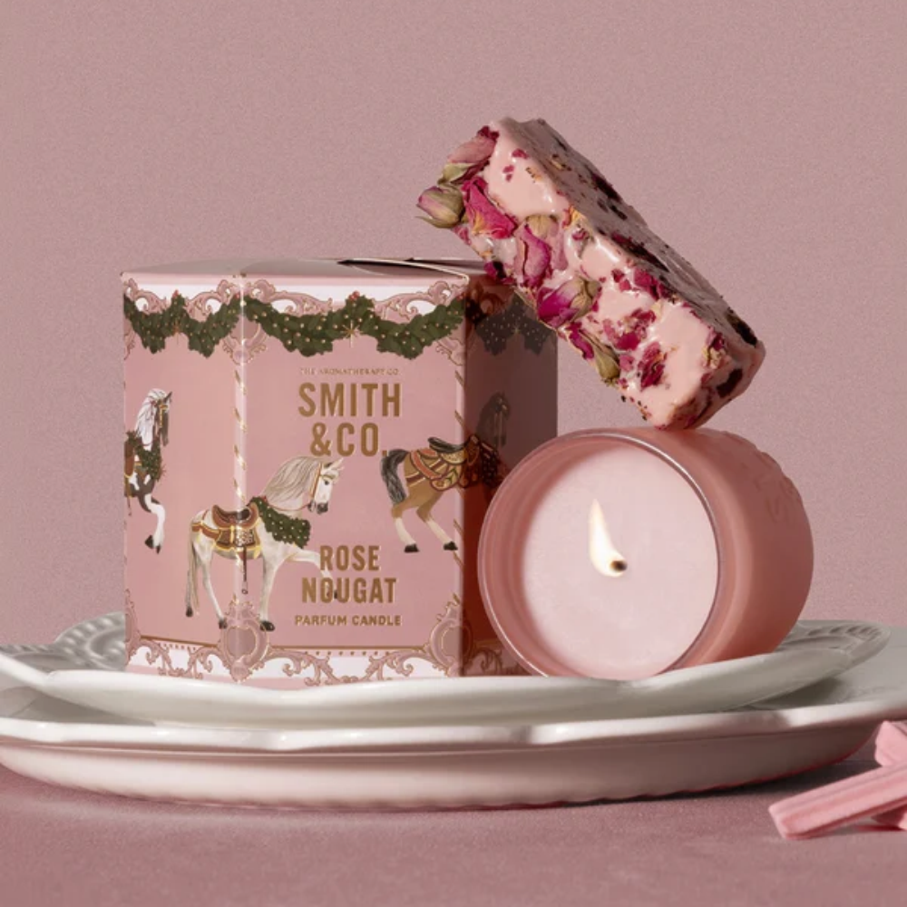 Lit Smith & Co. Rose Nougat candle on white plates beside its pink gift box topped with wrapped nougat