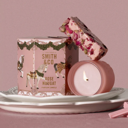 Lit Smith & Co. Rose Nougat candle on white plates beside its pink gift box topped with wrapped nougat