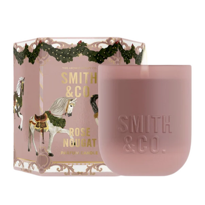 Smith & Co. Rose Nougat scented candle in a matte pink vessel beside its festive carousel horse gift box