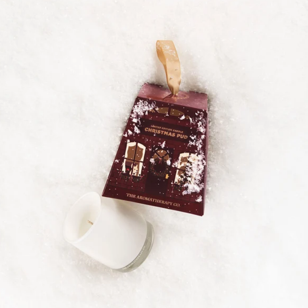 Therapy Christmas Pud gift box with a gold ribbon and white candle on a soft white faux fur throw